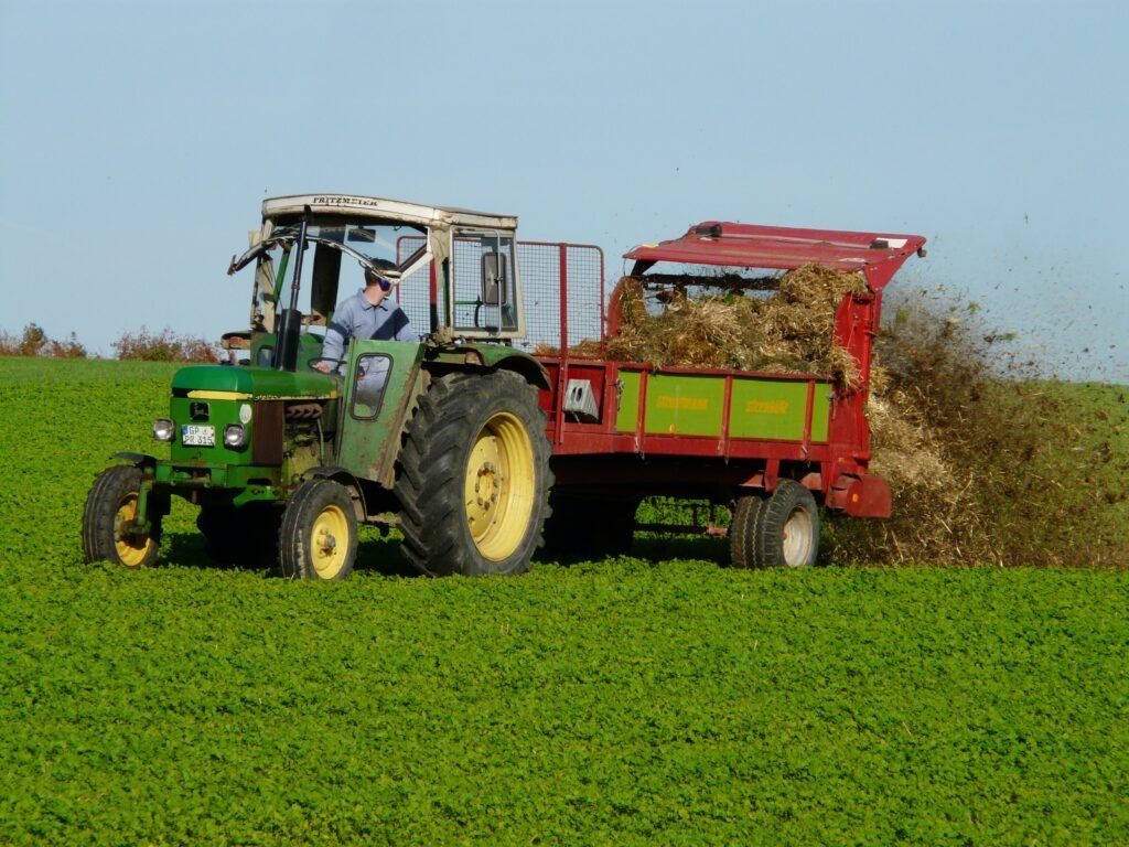 A farmer spreading organic compost or mulch in a green field.