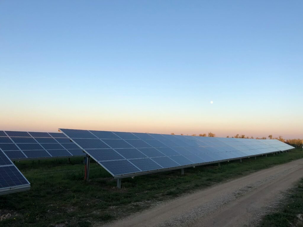 A scenic landscape of numerous solar panels arranged in neat rows across a vast open field, bathed in the warm orange glow of a sunset sky with scattered clouds. This copyright-free Pexels photo evokes sustainable energy themes relevant to solar-powered vertical farming.